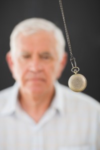Senior man being hypnotized with pendulum over black background